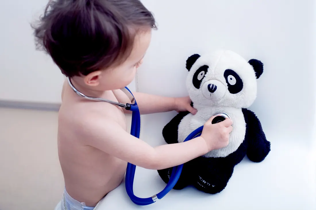 Toddler listening to a stuffed panda's heartbeat with a stethoscope